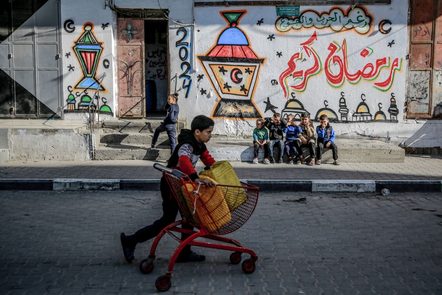 طفل يدفع عربة أمام جدار يحمل رسومات رمضانية في مدينة غزة (تصوير: ا ف ب)